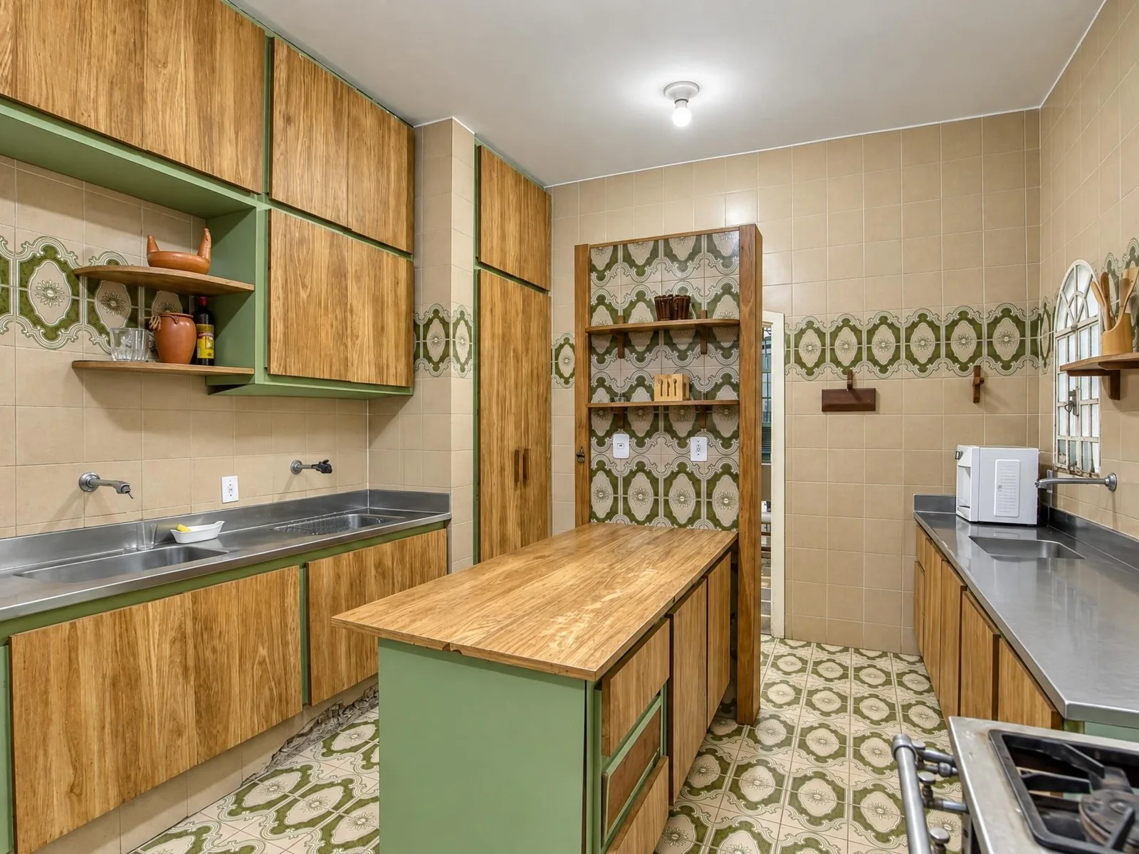 Cozinha da Casa Mares, com ilha de madeira, bancadas de inox e azulejos verdes