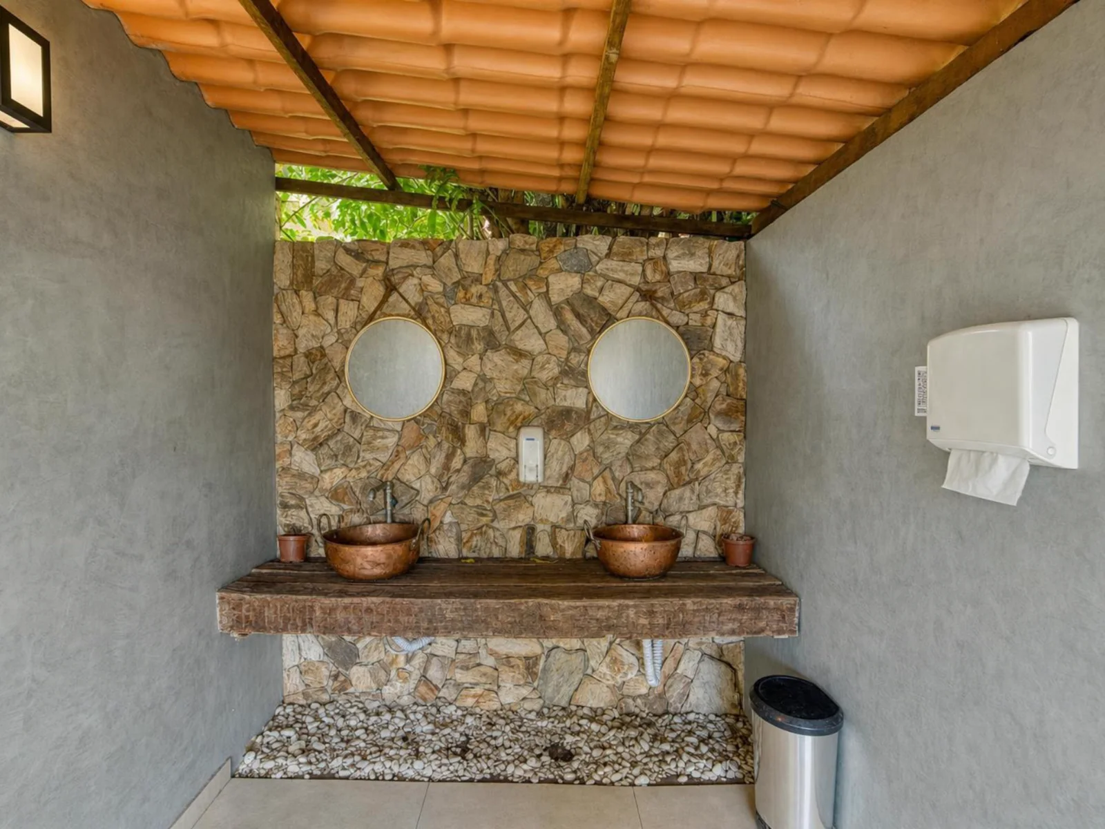 Parede de pedra com cubas de cobre e espelhos nos banheiros de evento