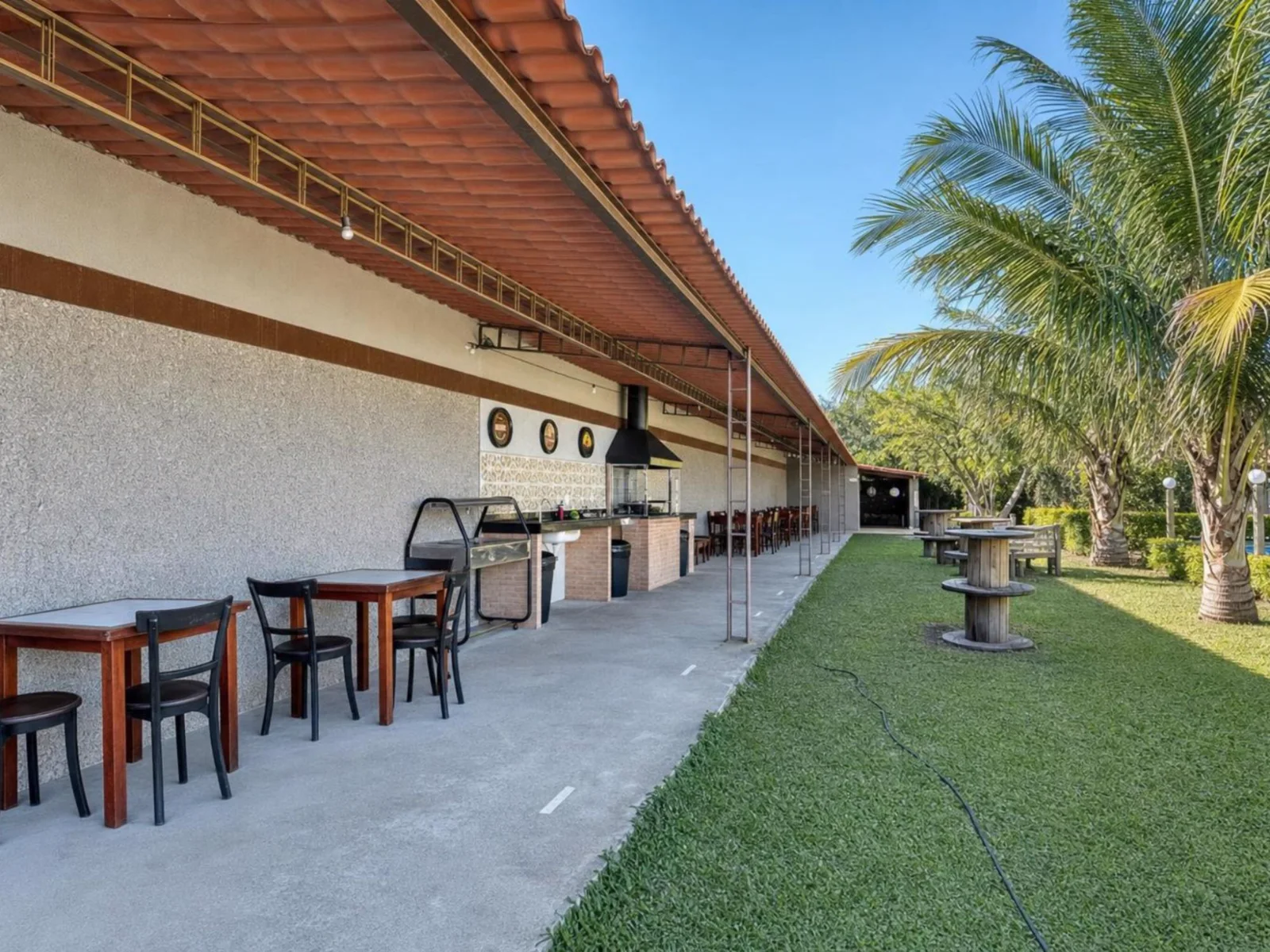 Área gourmet coberta com mesas de madeira e cadeiras