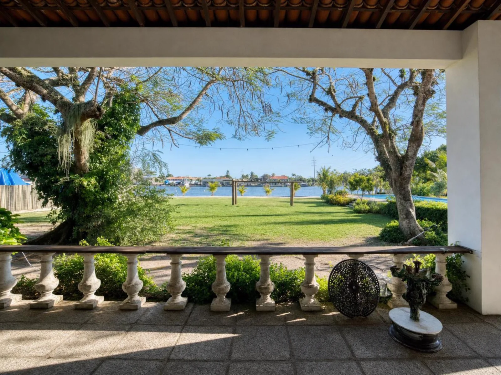 Varanda colonial com balaustrada aberta para o gramado, a pérgola e a lagoa